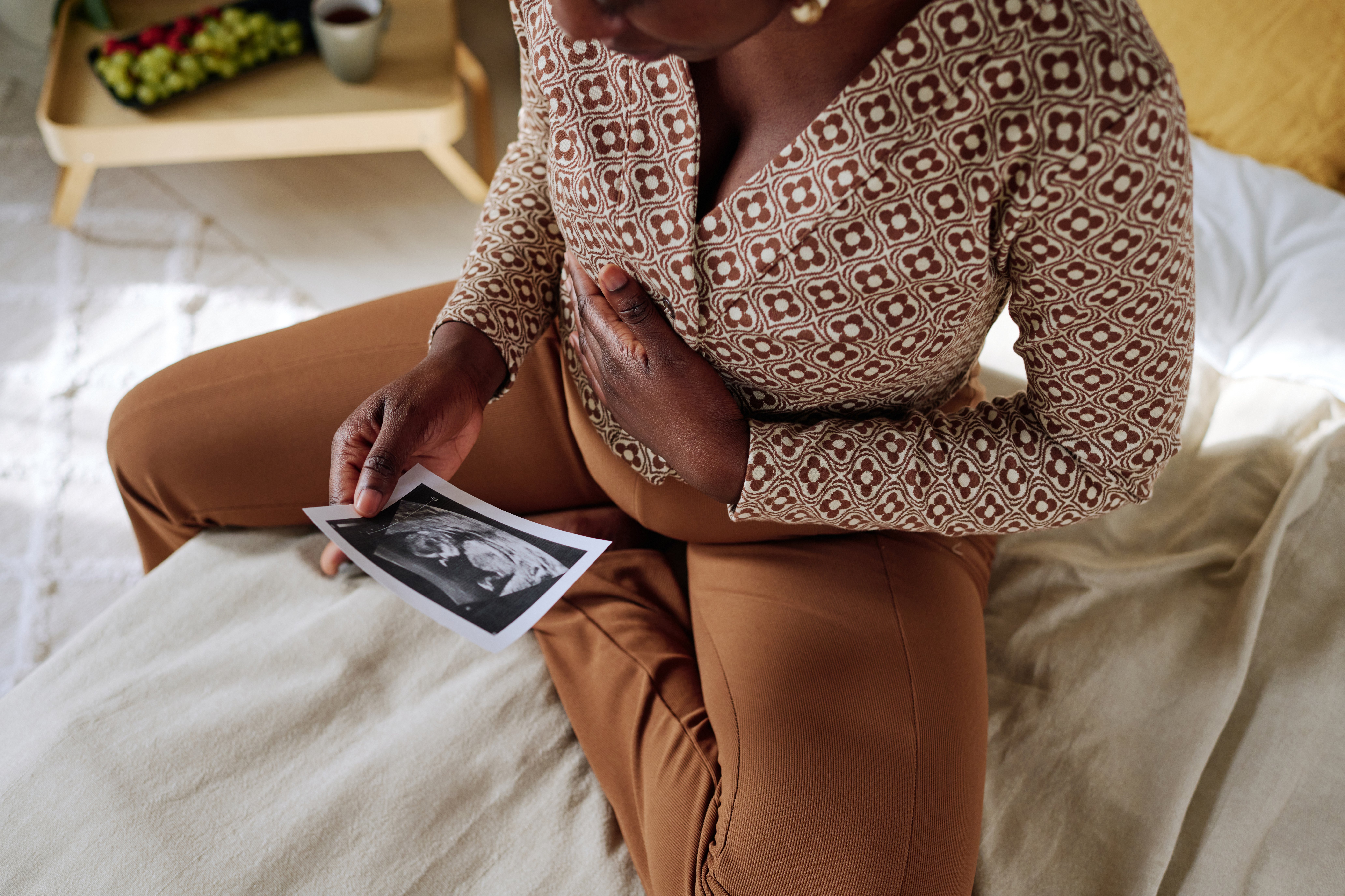 Close-up of African pregnant woman sitting on bed and examining the ultrasound of her baby